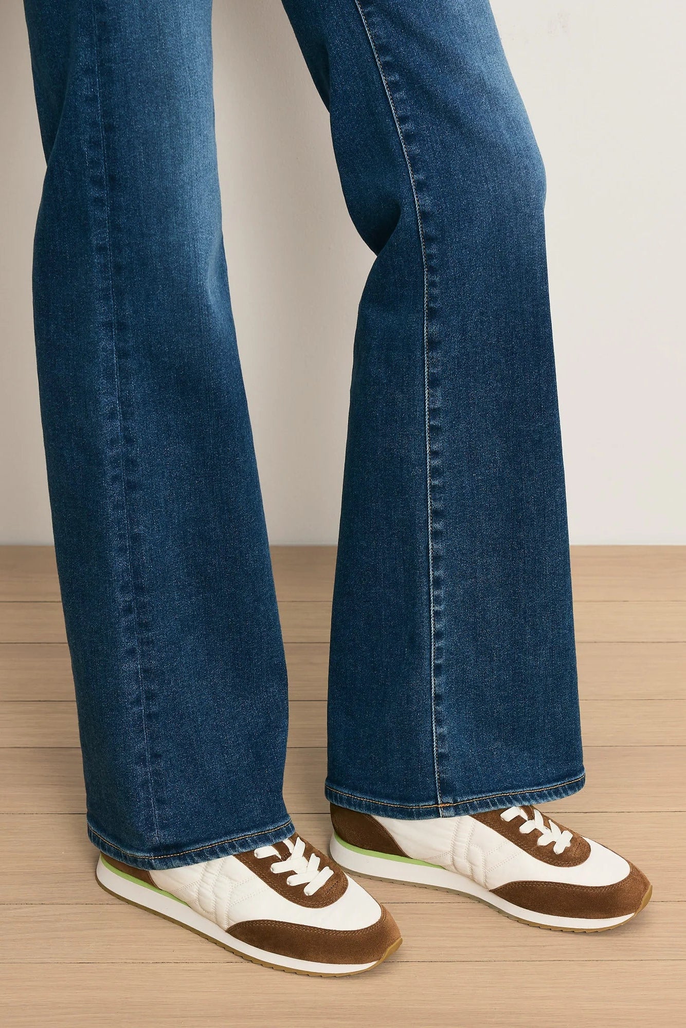 Person wearing blue jeans and brown and white sneakers on a wooden floor.
