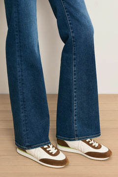 Person wearing blue jeans and brown and white sneakers on a wooden floor.